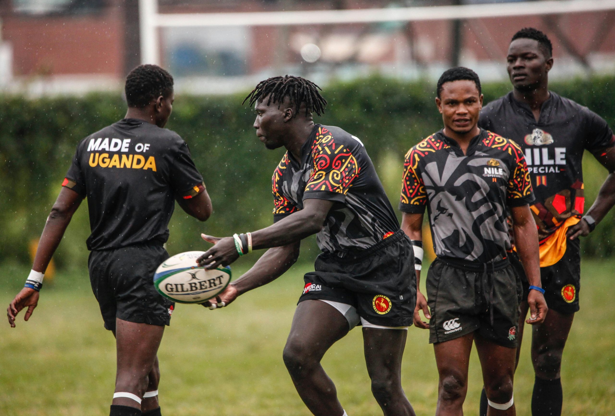 Rugby match featuring African players in Uganda-themed uniforms playing under rainy conditions.
