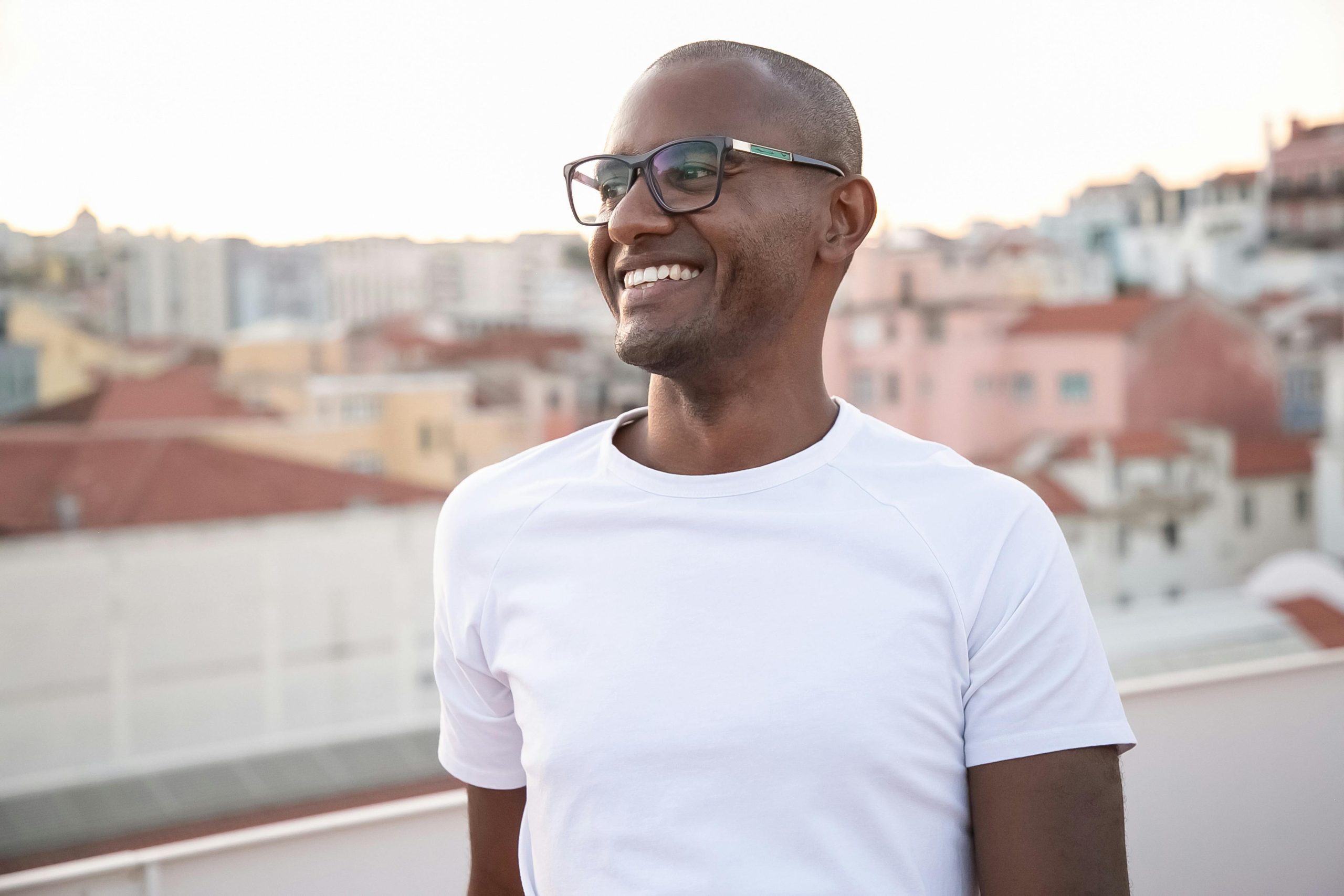 African American man smiling in white shirt with cityscape backdrop.